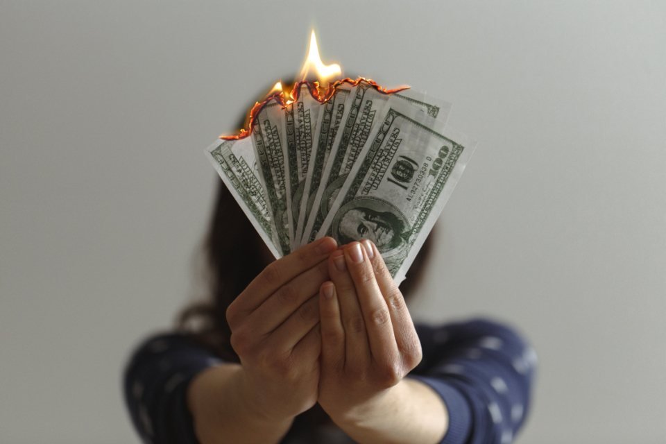 Person holding burning hundred dollar bills, illustrating the cost of hiring the wrong contractor