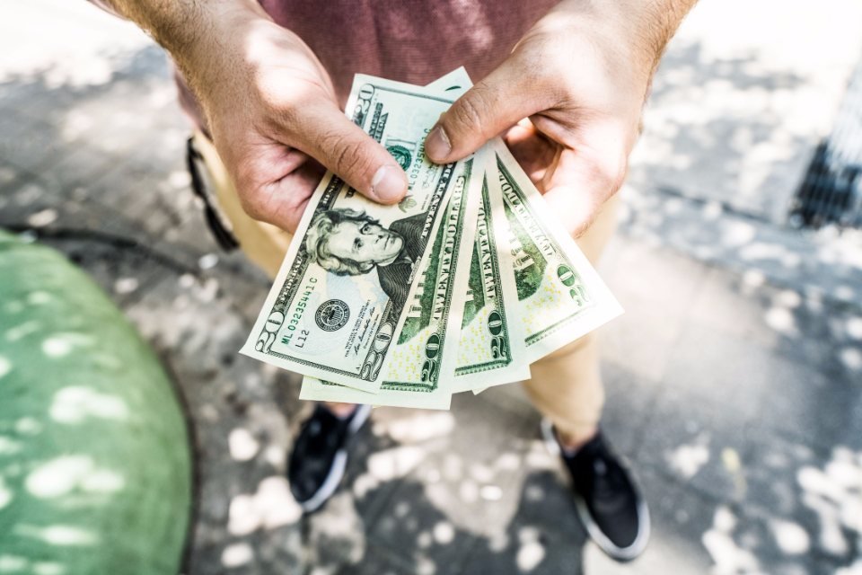 Hands offering a fan of twenty dollar bills, illustrating the cash-only payment red flag