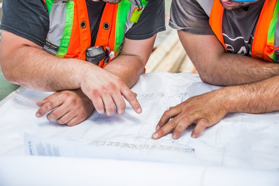 Two contractors in safety vests reviewing construction blueprints together before a project