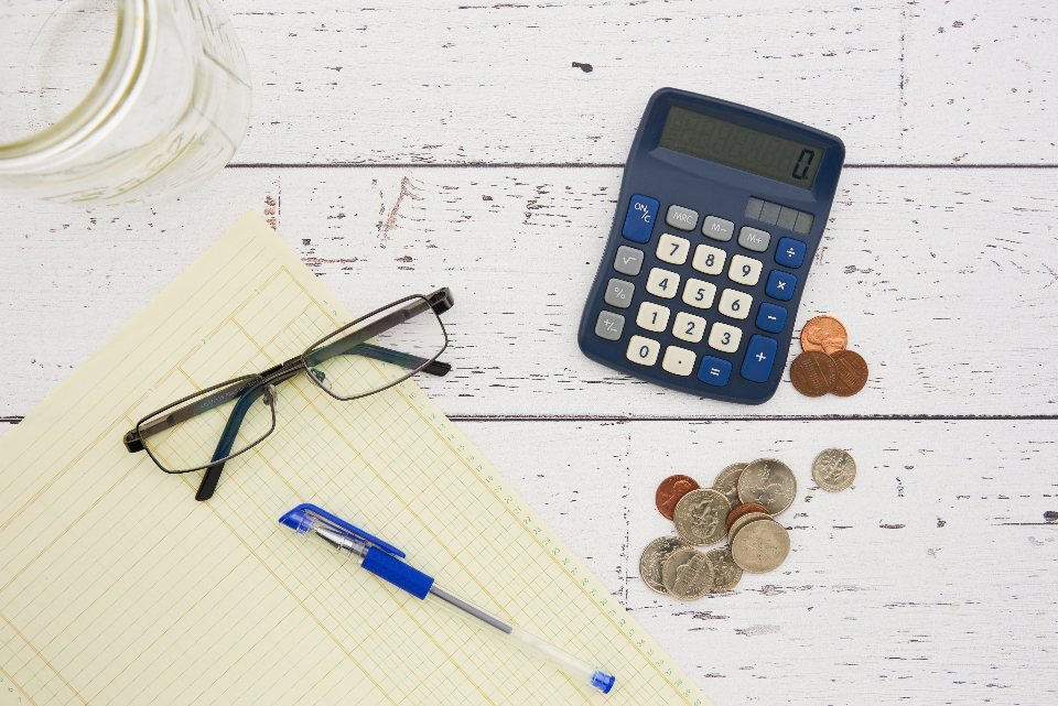 Calculator, ledger pad, and coins laid out for working through a contractor payment schedule
