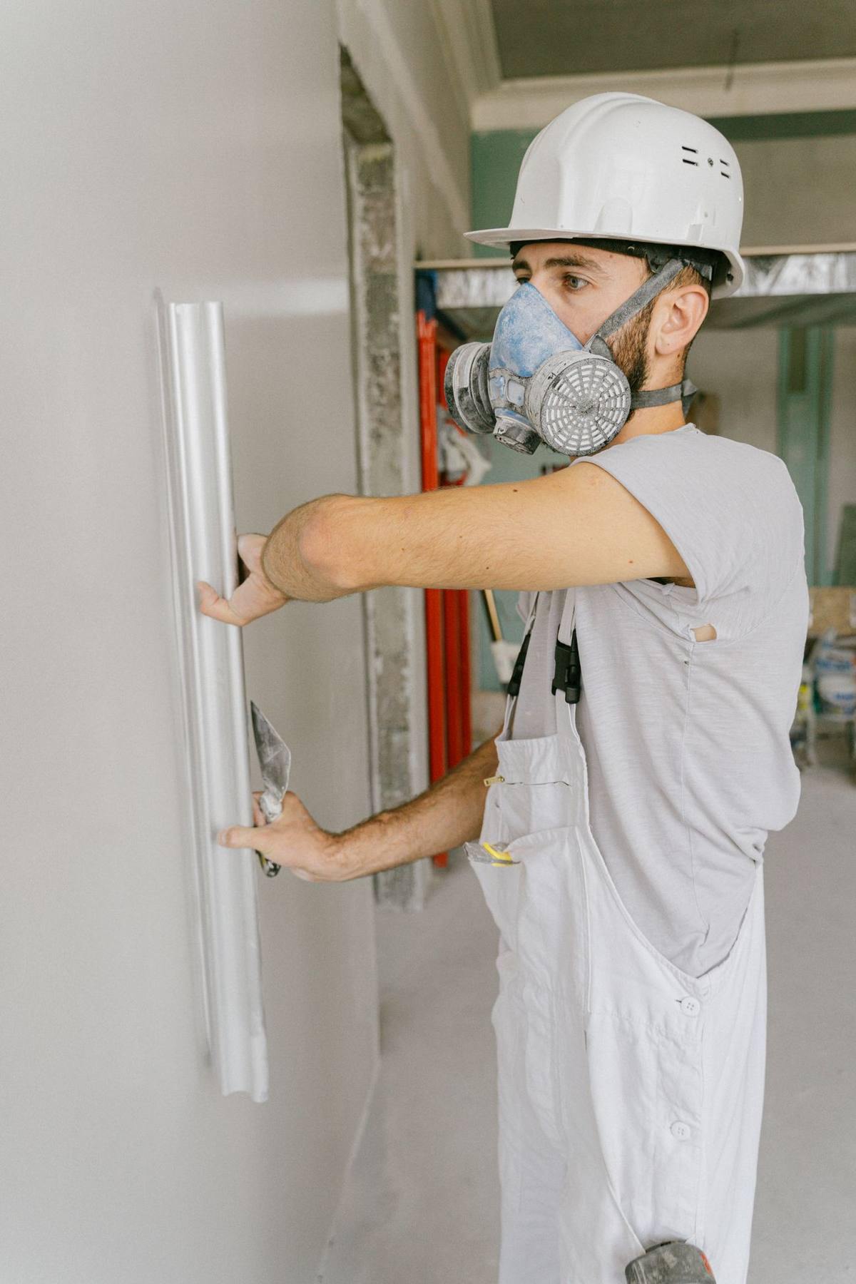 A drywall finisher in a respirator skim-coating a wall smooth with a plastering trowel