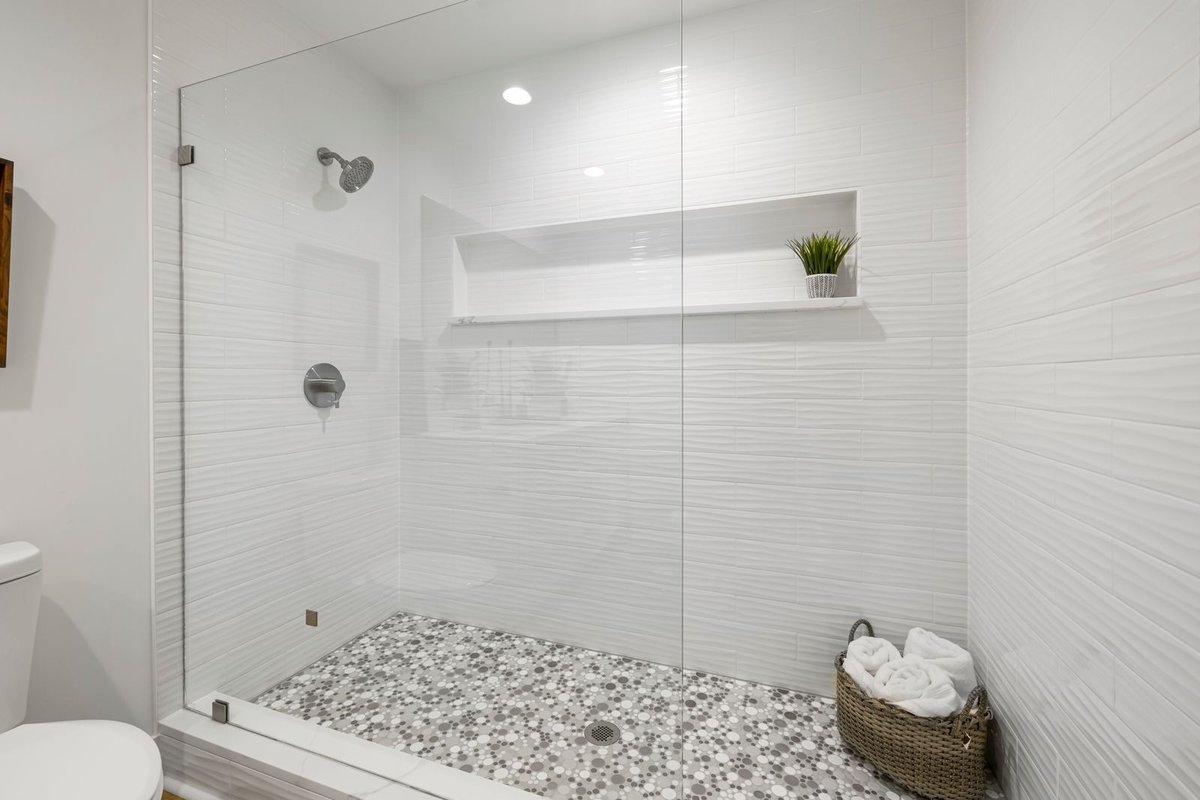 Penny-round mosaic shower floor sloping to a center drain in a glass walk-in shower
