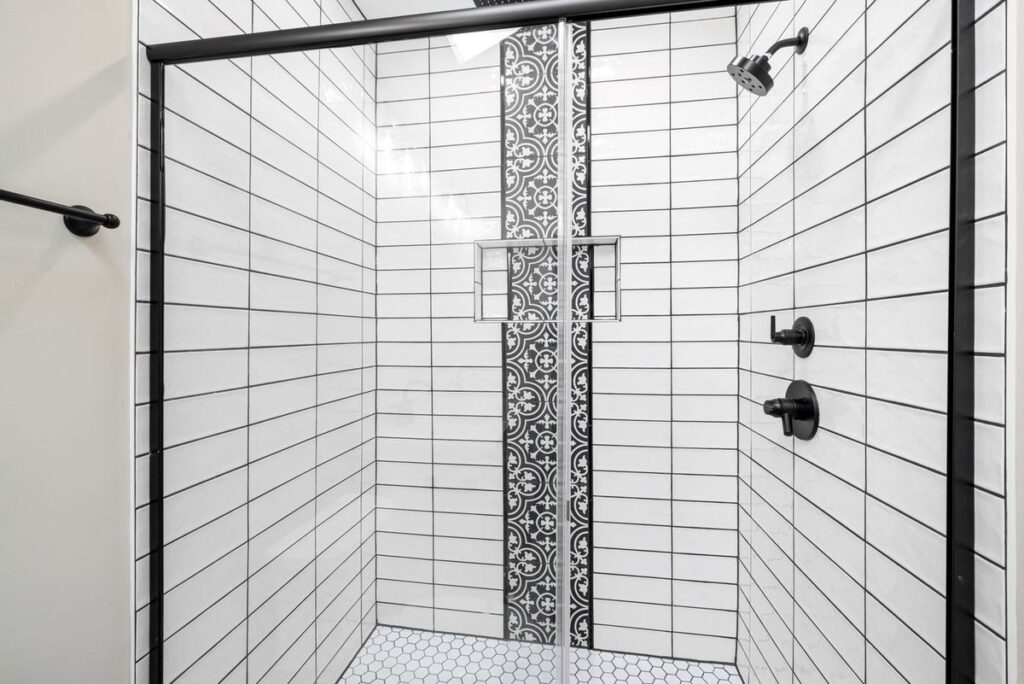 White subway tile shower with dark grout lines, a glass door, and a hex-tile floor showing the joints a regrout renews