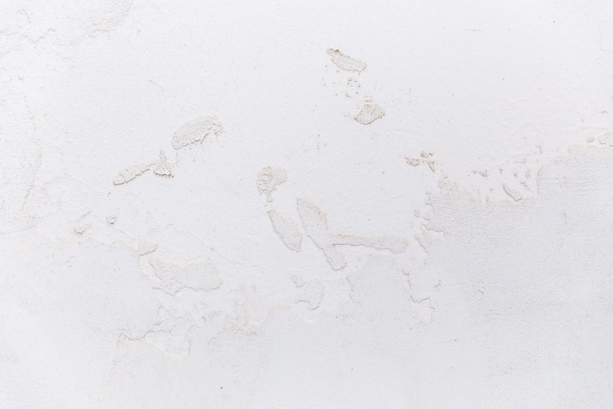 A white stucco wall showing patchy surface damage and shrinkage cracking